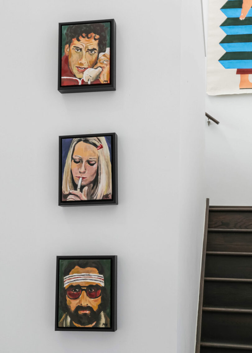 Three pieces of are on a wall before a stairway.