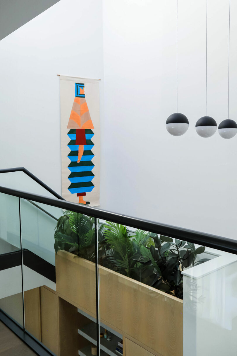 Looking back down a hall to a stairway. Art is visible in the double height space.