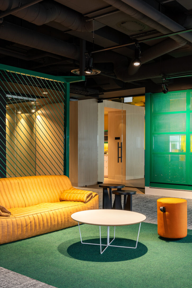 An lounge area with a green rug, yellow sofa, and white table.