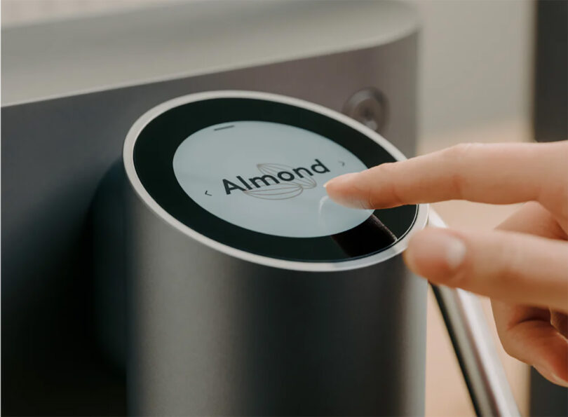 A person reaching with one finger across the nunc.'s touchscreen display showing the machine's almond milk setting.