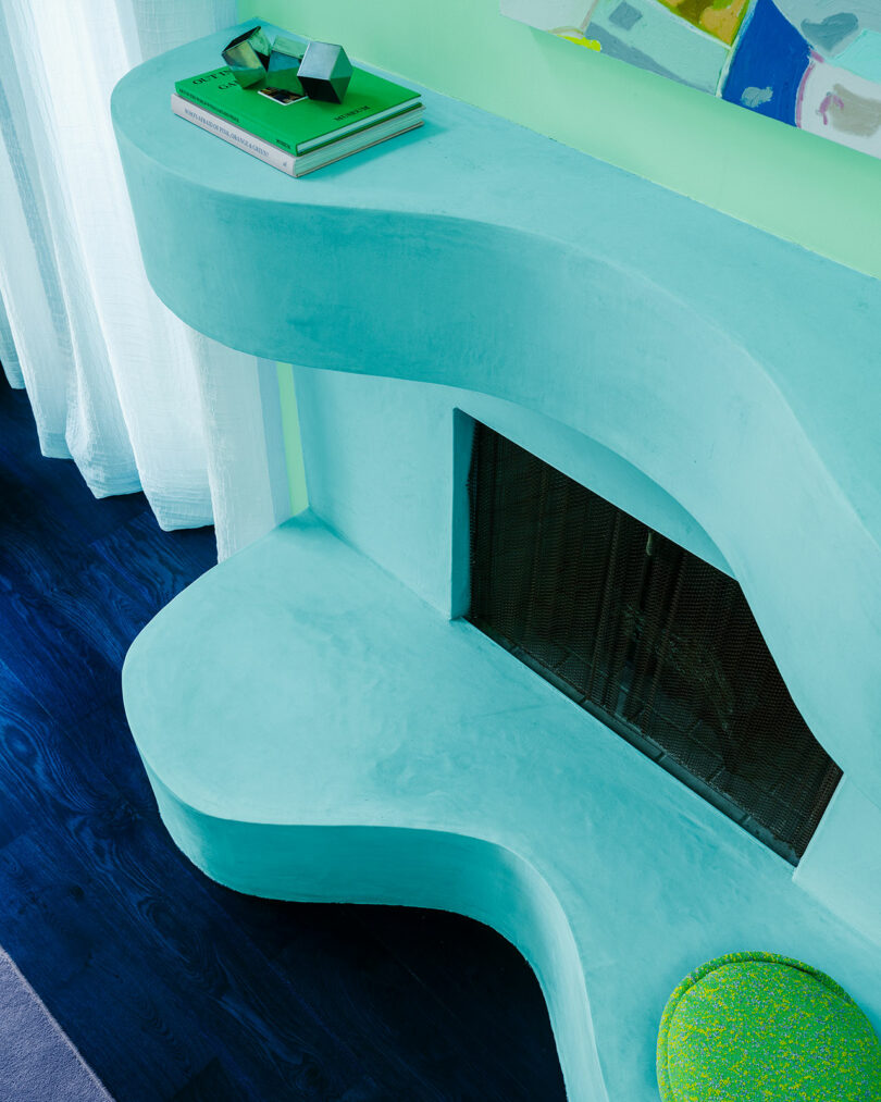 A soothing turquoise curved fireplace mantle and hearth in a contemporary room with sheer white curtains and a dark blue floor.