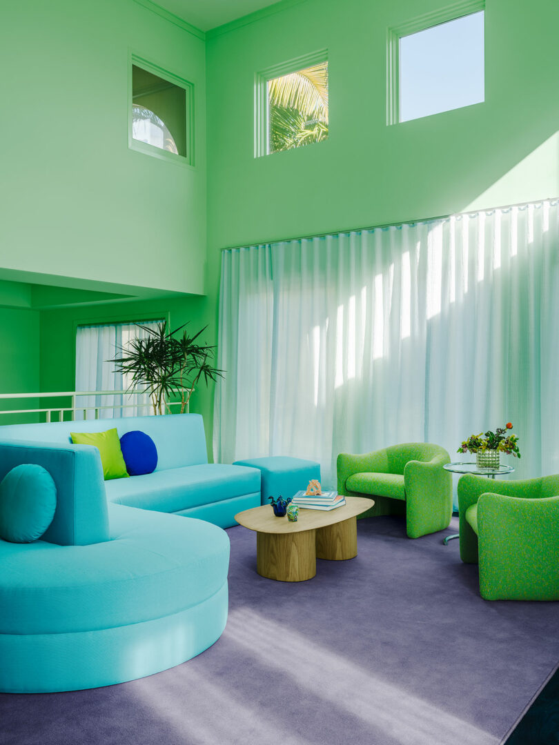 A vibrant living room with a blue fireplace, green furniture, light green walls, and sheer curtains.