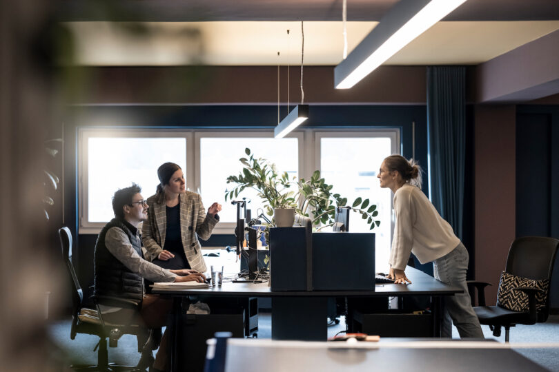 Three NOA professionals engaged in a discussion in a modern office space.
