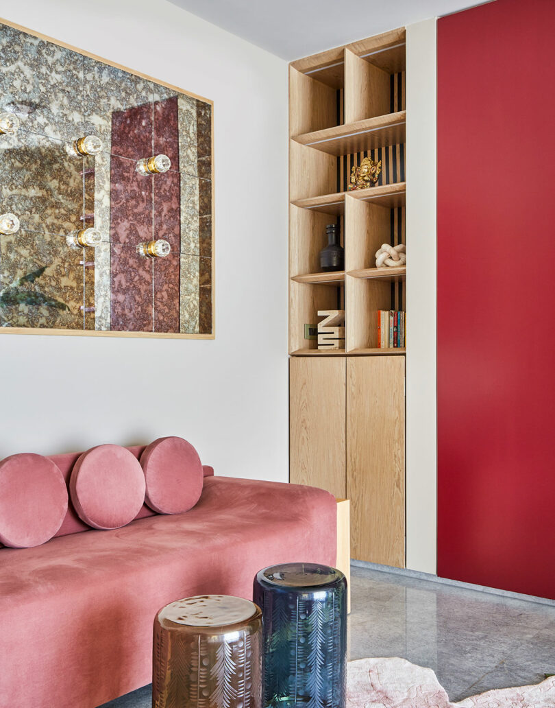 A modern lounge space featuring a pink velvet sofa, a wooden bookshelf, and an ornate marbled wall panel.