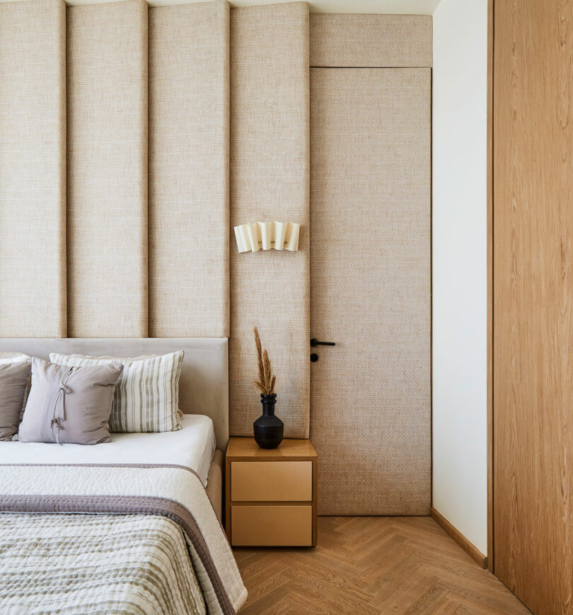 A cozy bedroom corner with a concealed door seamlessly integrated into the wall paneling, next to a neatly made bed with textured bedding and a small side table.