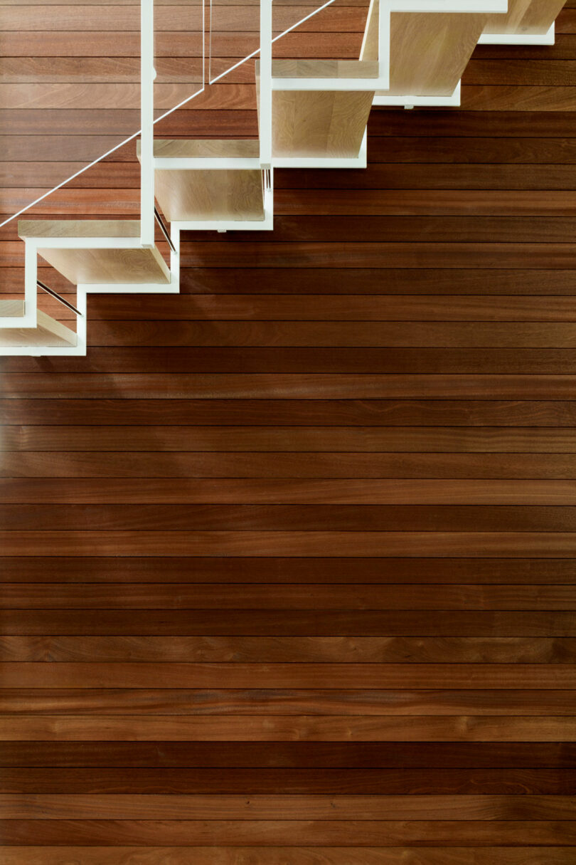Modern wooden staircase with white balustrade on a hardwood floor.