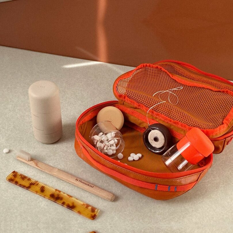by Humankind Best Sellers Set with the deodorant, a tooth brush, a toothpaste tablet and hair comb on the counter, and the toothpaste tablet container and floss in a red travel bag